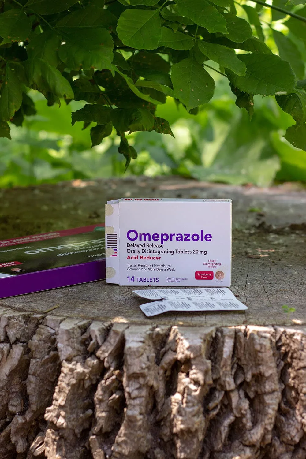 Omeprazole package sitting on a tree stump under leaves. 