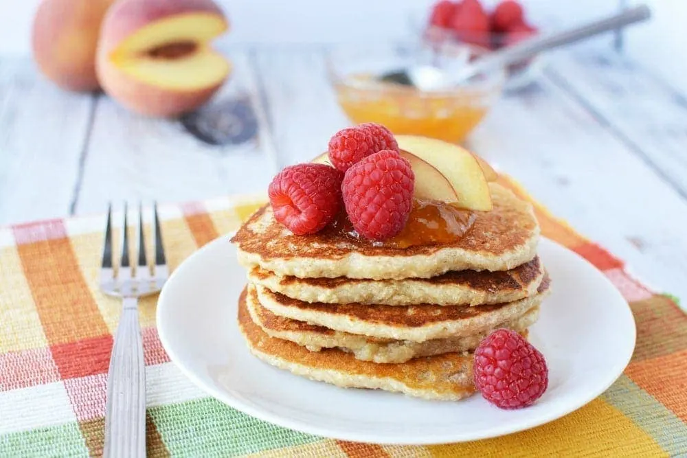 Stack of pancakes topped with peaches and raspberries. 