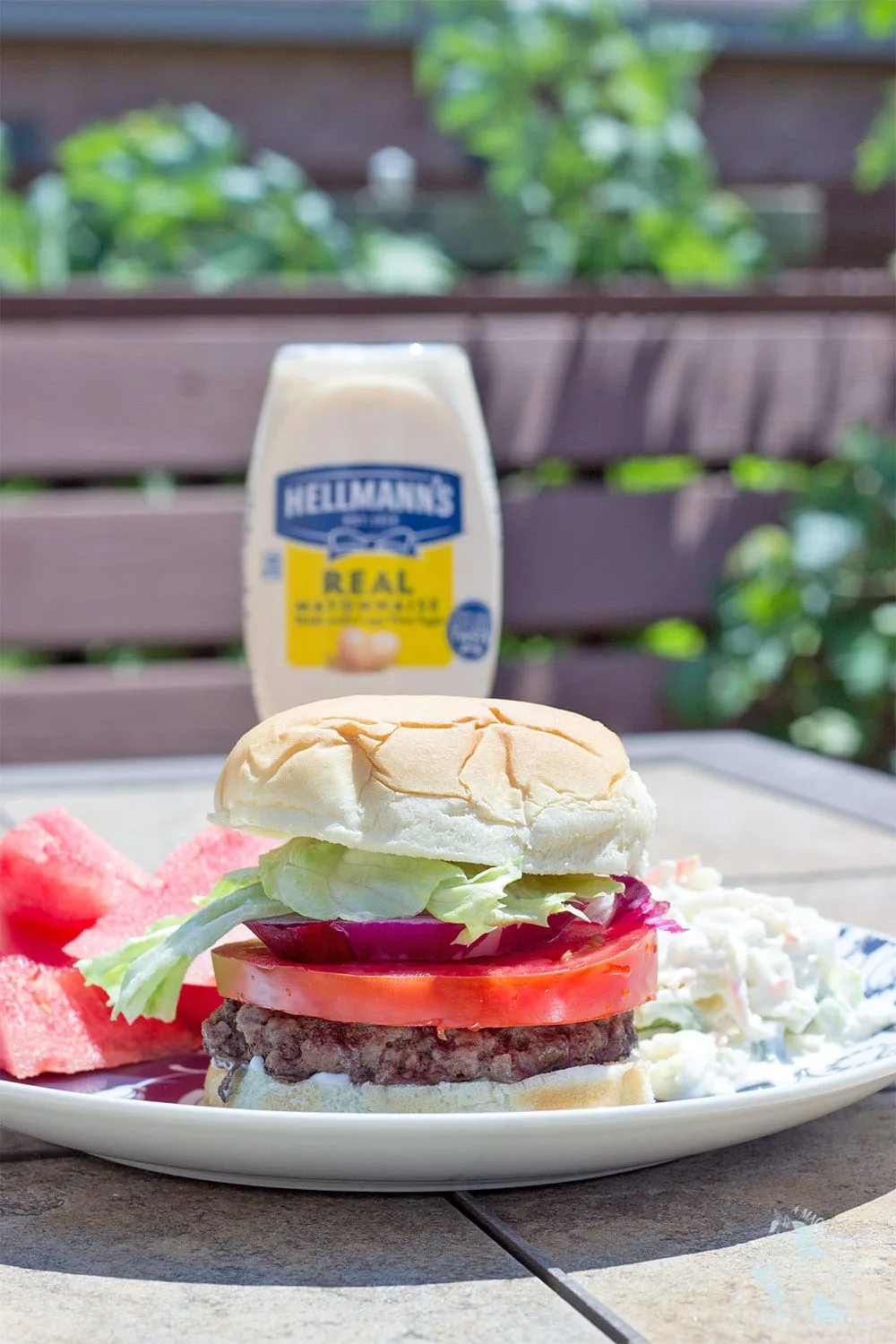 A burger with lettuce, tomato, and onion on a plate with mayo in the background.