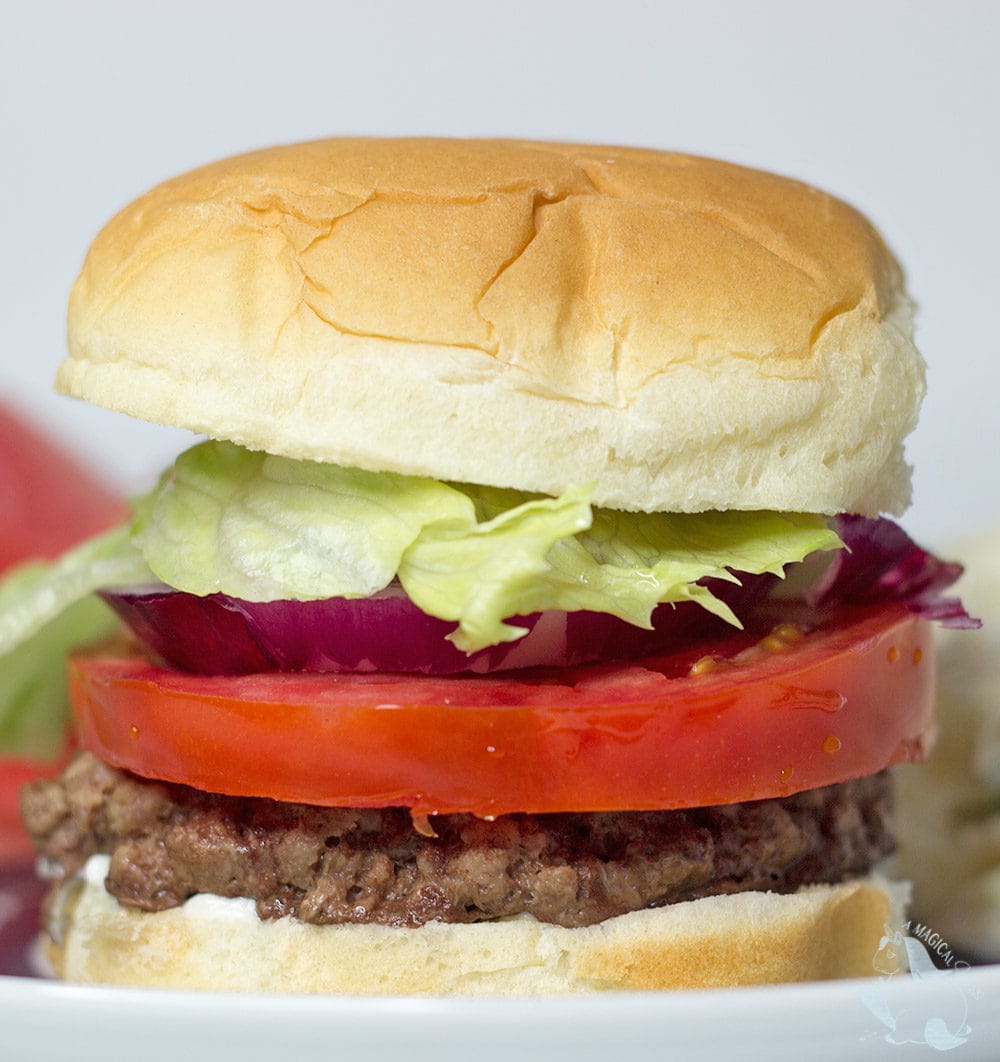 A burger with lettuce, tomato, and onion stacked on a plate.