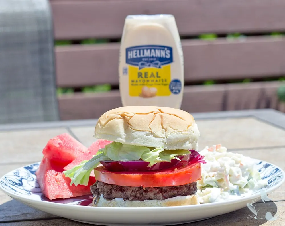 Burger, coleslaw, and watermelon on a plate on a patio table outside. 
