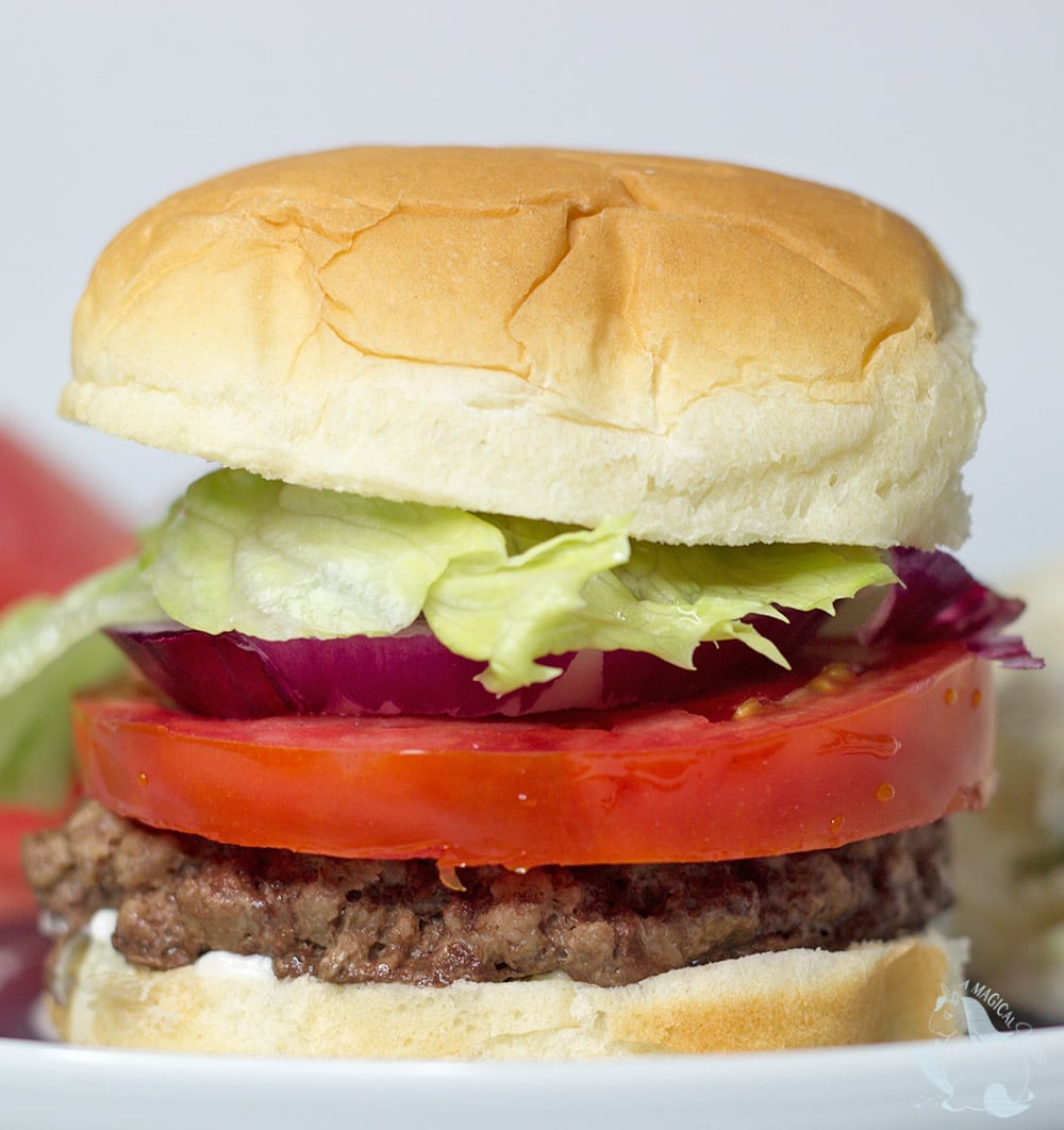 A burger with lettuce, tomato, and onion stacked on a plate. 