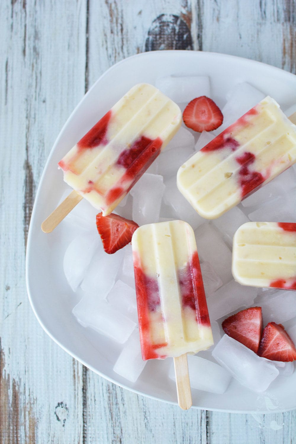 Strawberry popsicles in a dish with ice and fresh sliced strawberries.