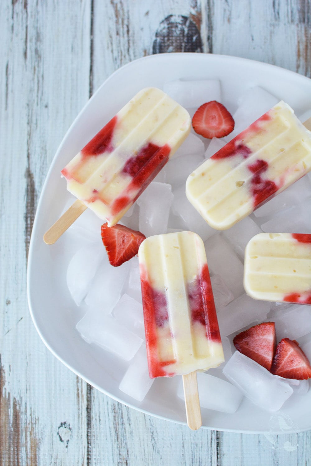 Strawberry popsicles in a dish with ice and fresh sliced strawberries. 