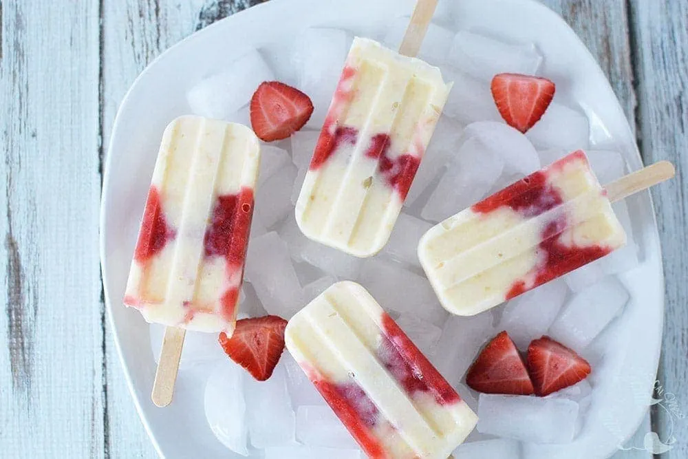Strawberry cheesecake pops in a bowl with ice and strawberries. 