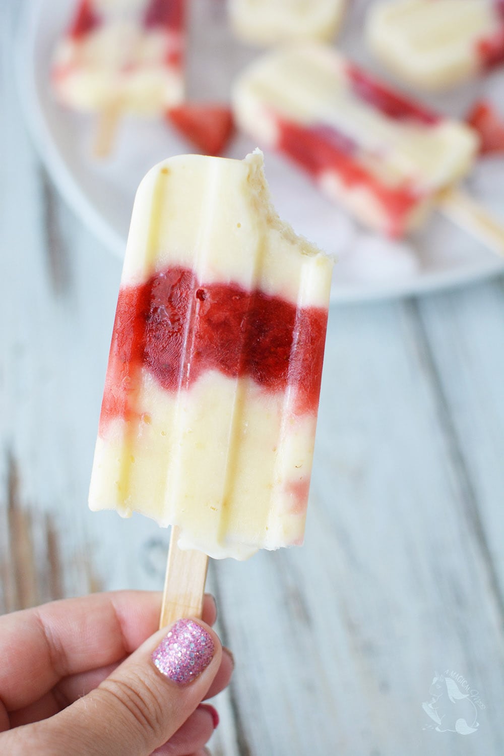 Holding a strawberry cheesecake pop with a bite taken out of it. 