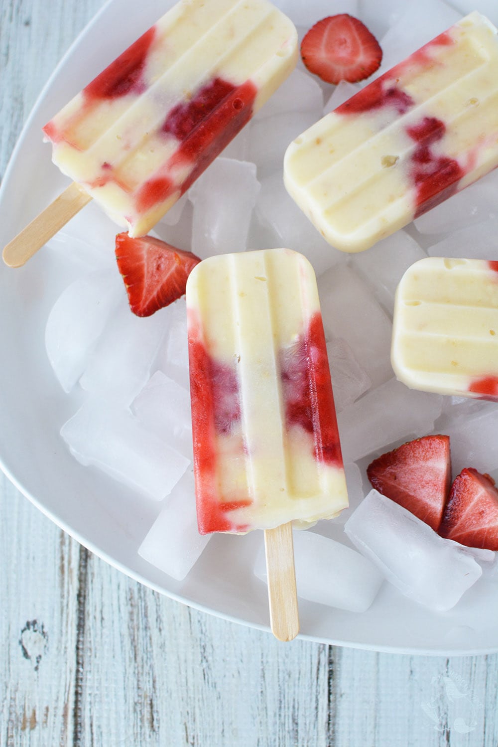Homemade ice pops lying on a bed of ice with strawberries