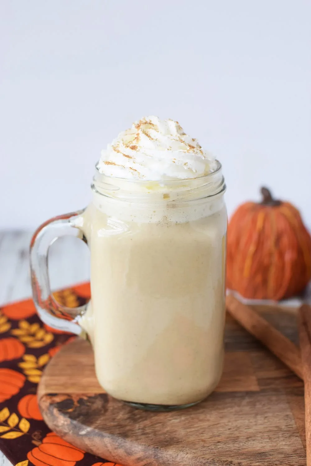 Pumpkin spice latte topped with whipped cream and cinnamon sitting by pumpkins.