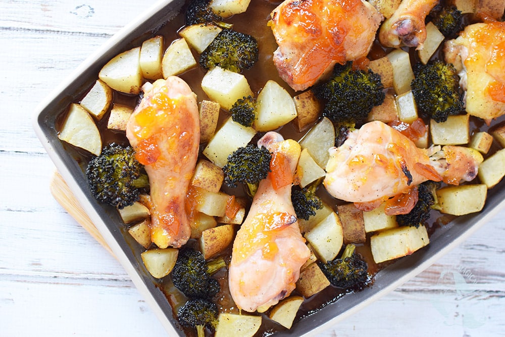 A sheet pan filled with chicken legs, broccoli, and potatoes, covered with a peach topping. 