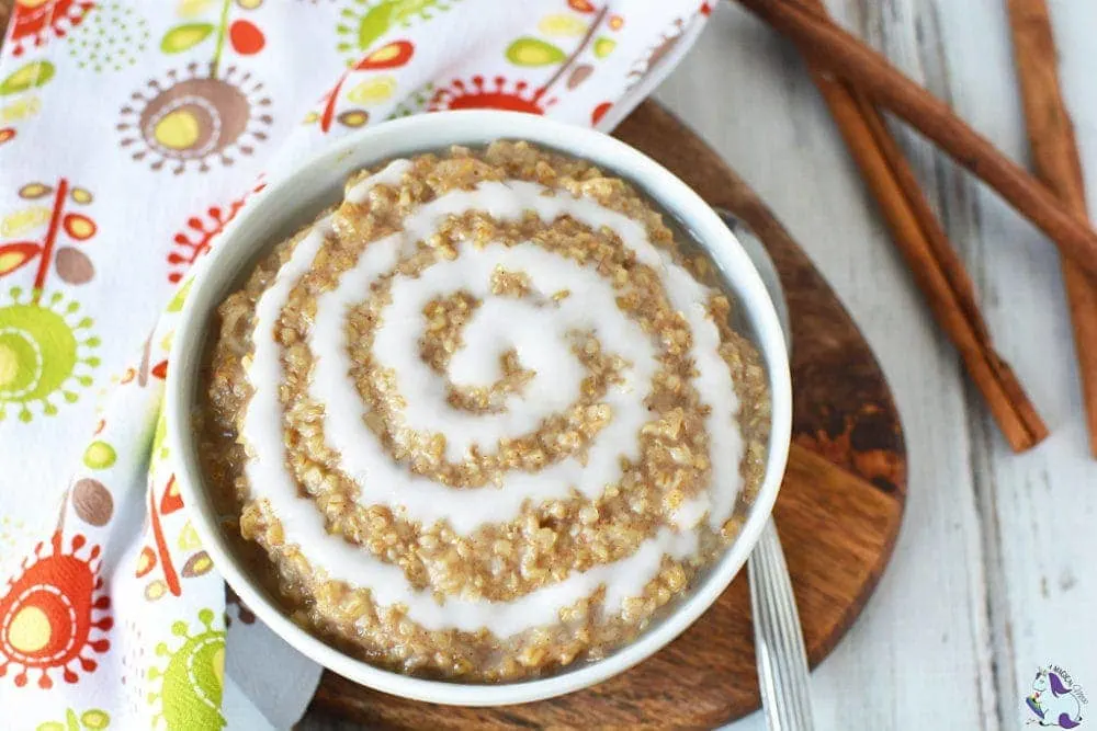 Bowl of oatmeal with a cinnamon roll swirl next to cinnamon sticks.