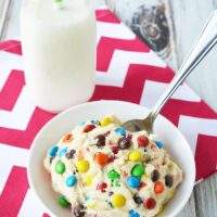 Cookie dough in a white bowl with a spoon and a glass of milk.