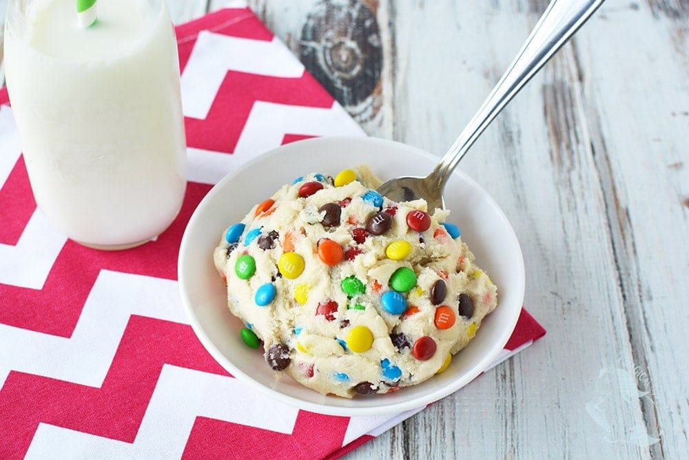 Cookie dough in a bowl with a spoon and a glass of milk.