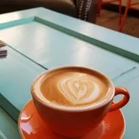 latte in an orange mug on a light blue table