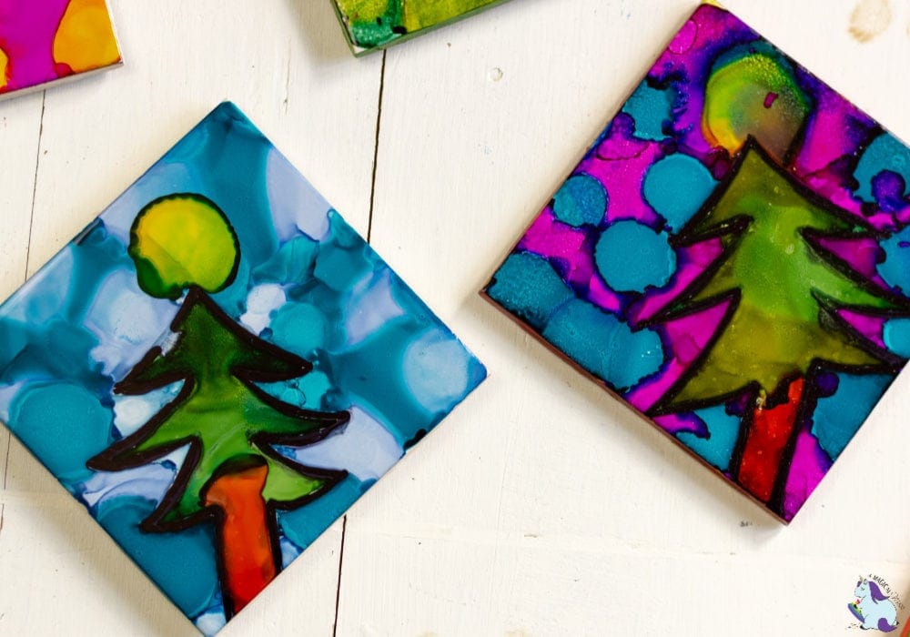 Two tiles decorated with alcohol ink with Christmas trees. 