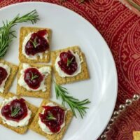 Cream cheese, cranberry jam, and fresh rosemary on a Triscuit