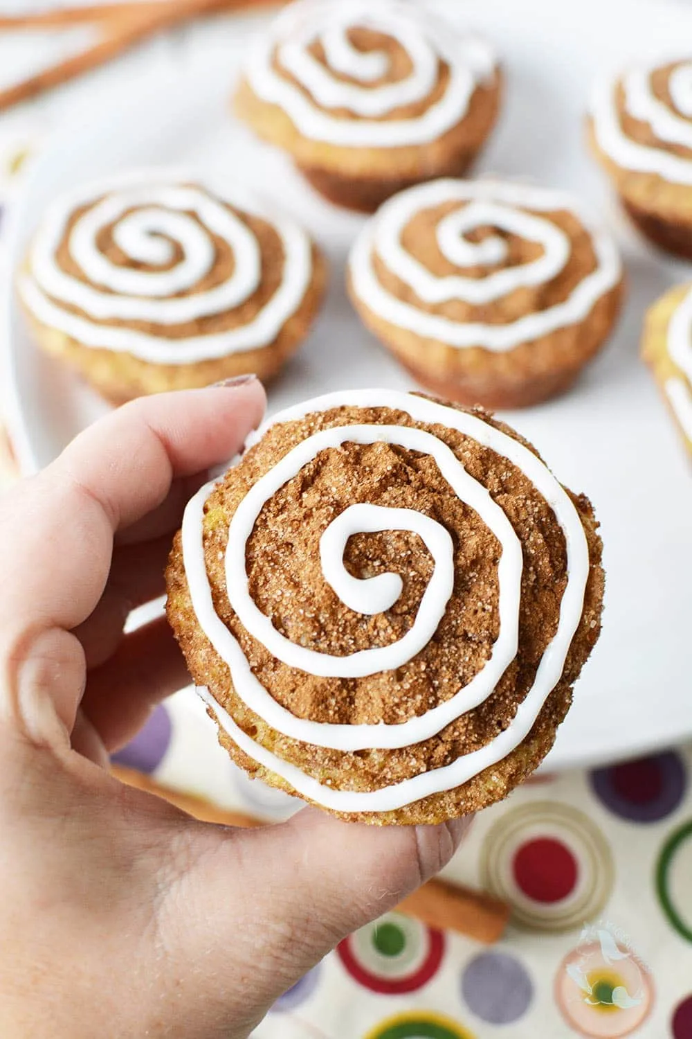 Holding a cinnamon roll muffin up to get a closer look of the glaze topping. 