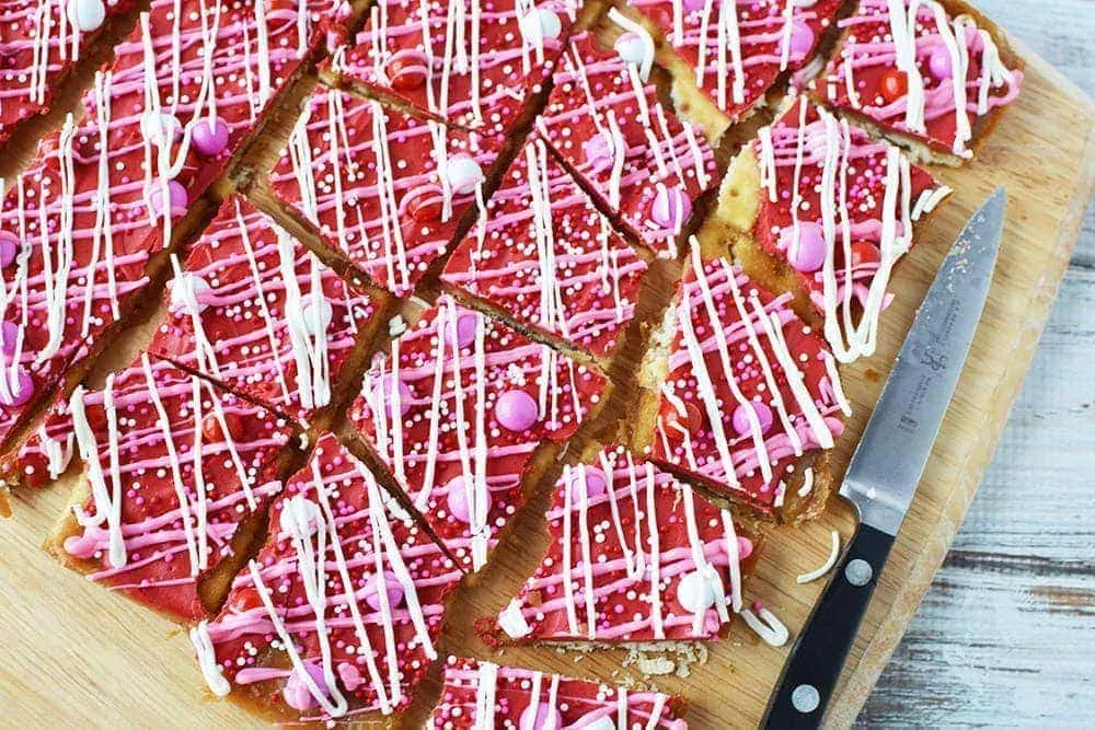 Crack candy with red and pink decorations on a cutting board with a knife. 