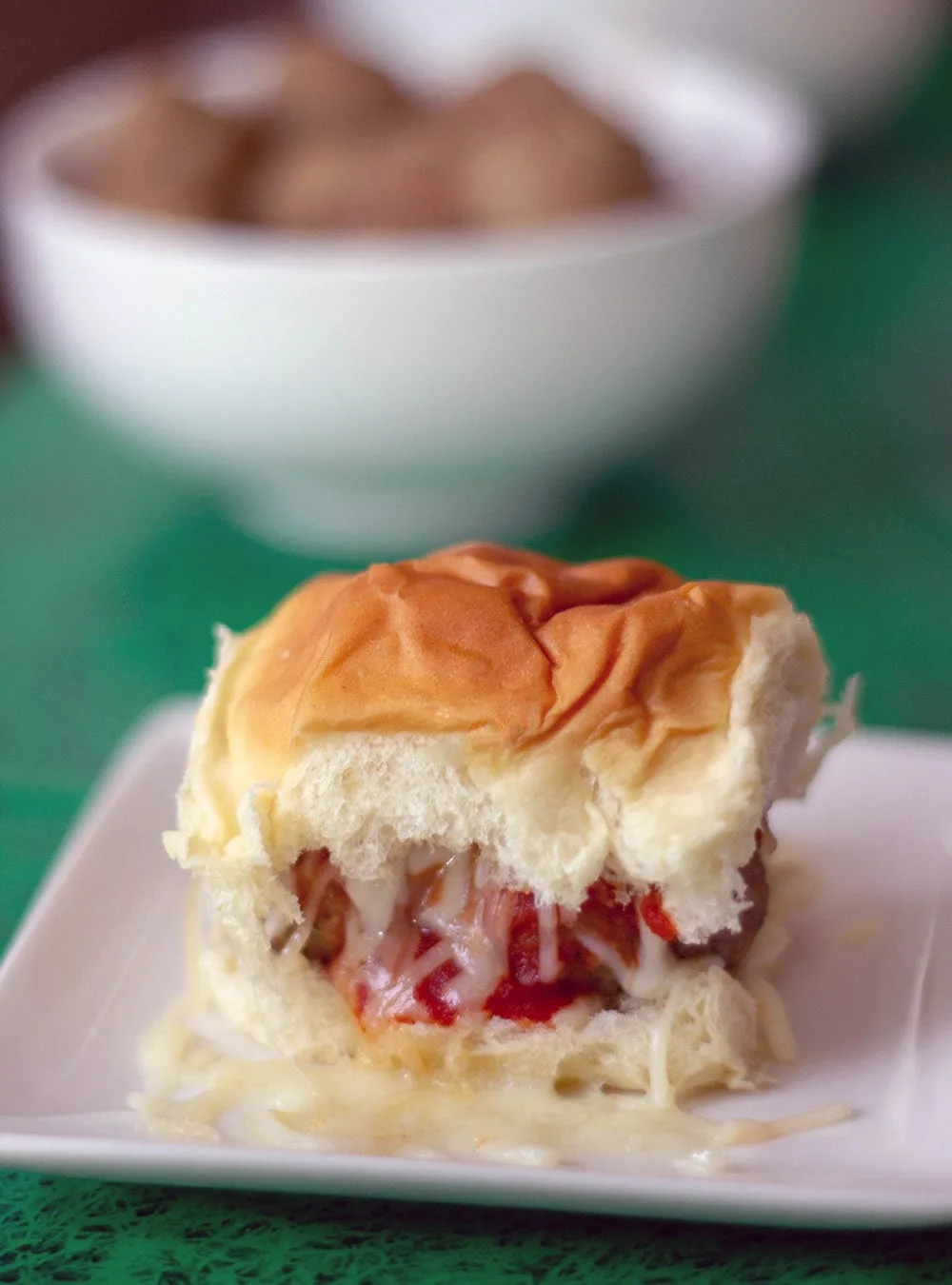 Meatball slider with bowl of meatballs in the background.