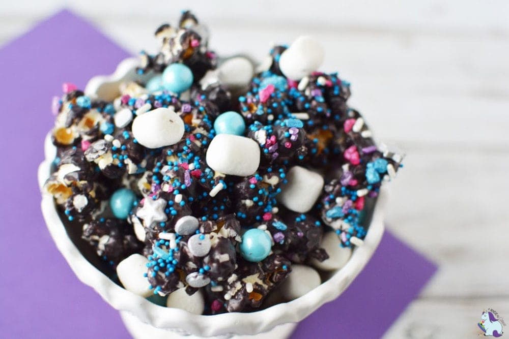 Dark purple candy covered popcorn with marshmallows and sprinkles.