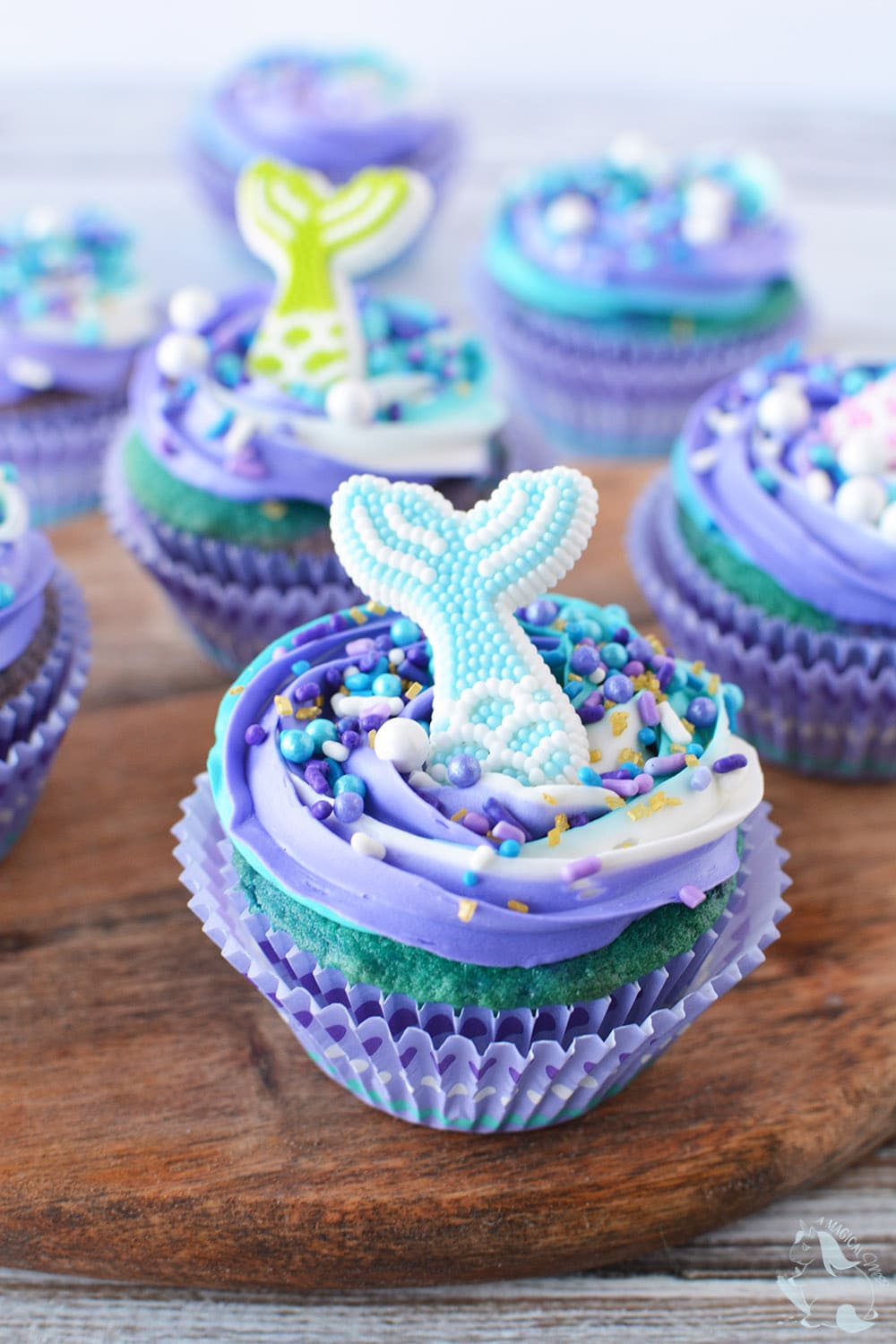 Mermaid cupcake sitting on a board with more cupcakes in the background.
