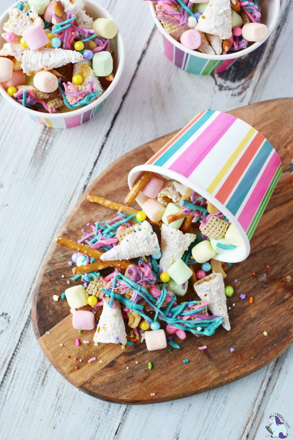 Unicorn party snack mix spilling out of striped paper cup on cutting board