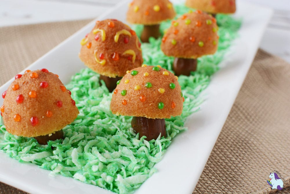 Little donut holes decorated like toadstools in edible grass on a white plate. 