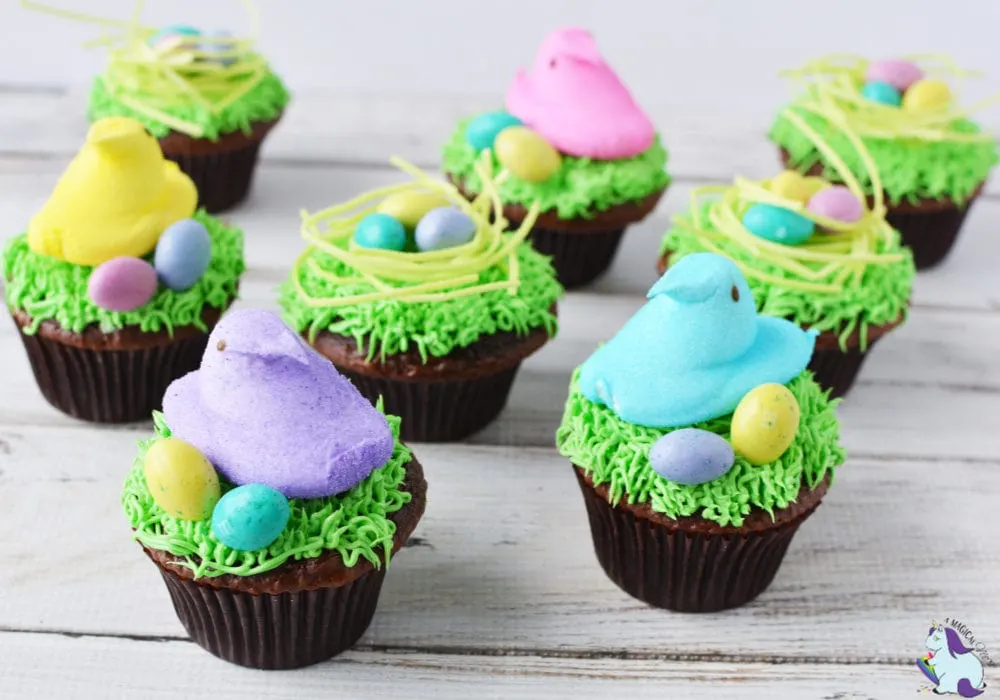 Chocolate cupcakes topped with edible grass, marshmallow Peeps, and candy eggs for Easter. 