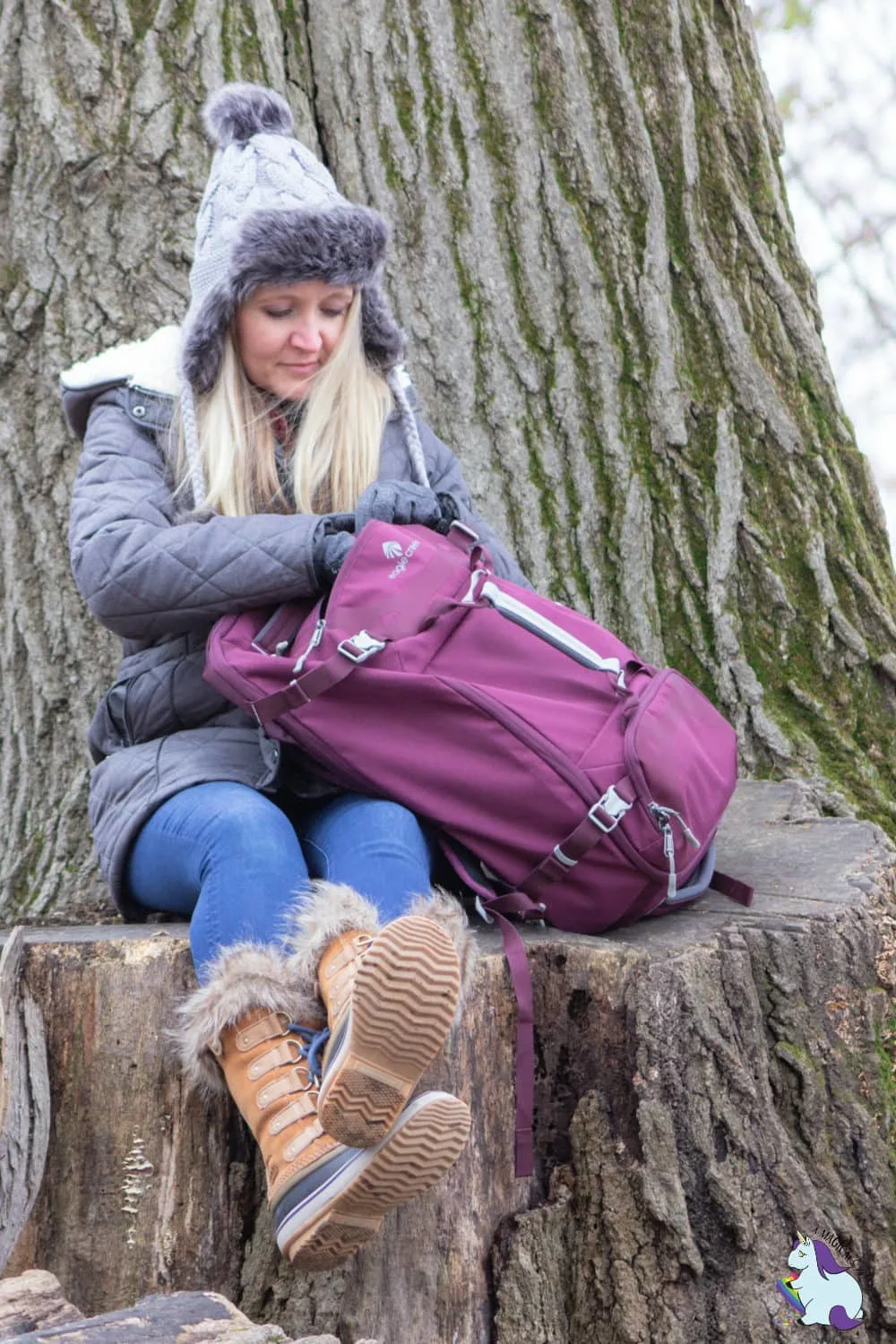 Shelley VanWitzenburg sitting on large tree stump with plum backpack