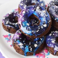 Galaxy donuts with star sprinkles stacked on a plate.