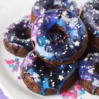 Galaxy donuts with star sprinkles stacked on a plate.