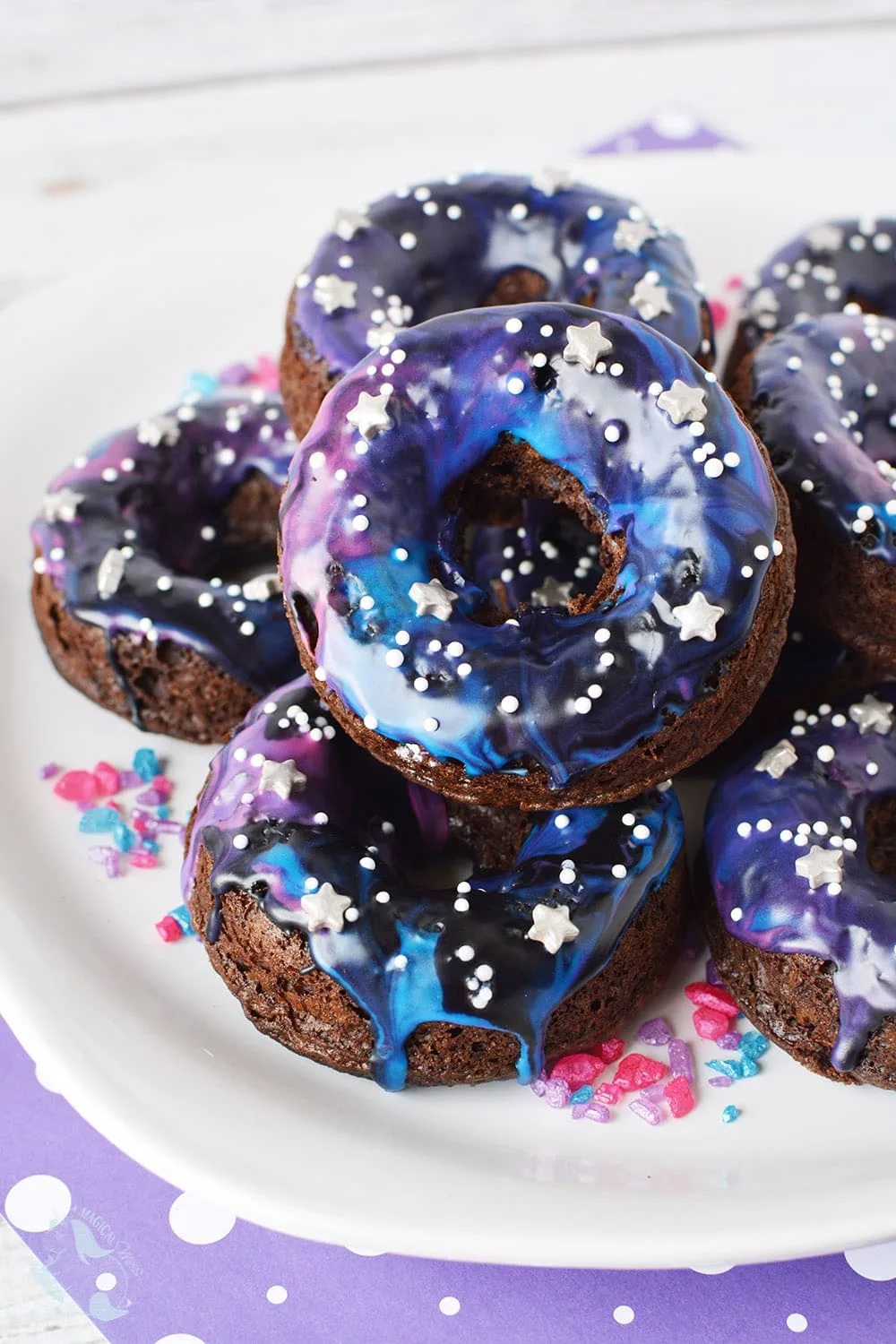 Galaxy donuts with star sprinkles stacked on a plate. 