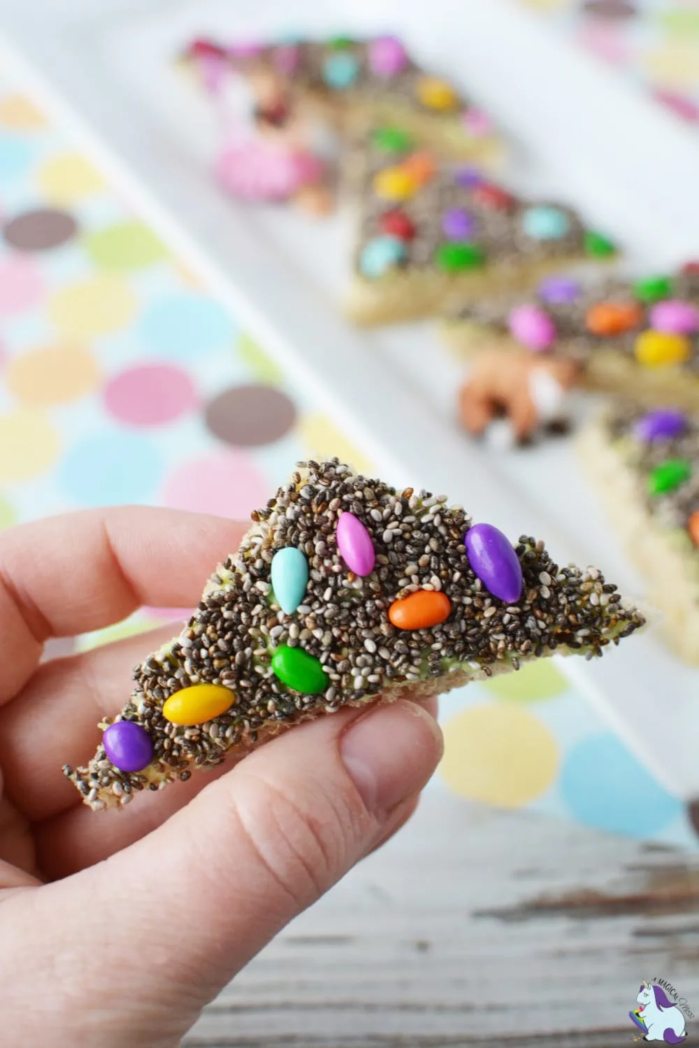 Holding a piece of bread that is covered in chia seeds and sunflower seeds. 