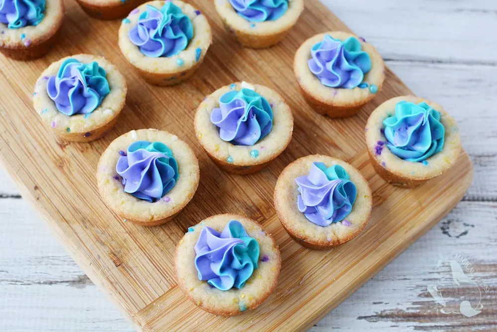 Filling cookie cups with purple and blue shades of frosting. 