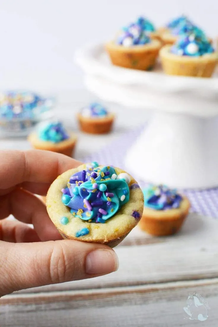Holding a cookie cup filled with blue and purple frosting and sprinkles.