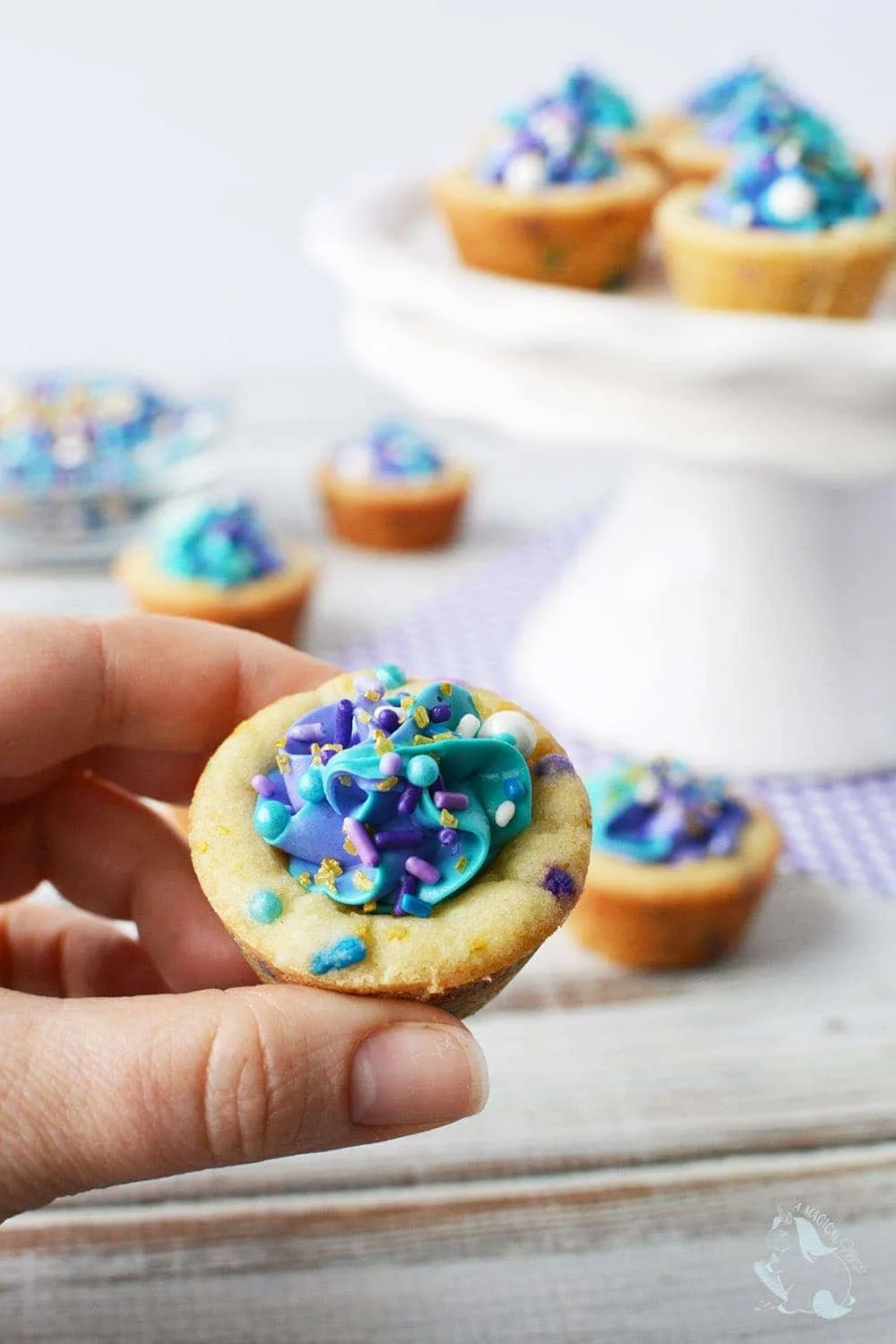 Holding a cookie cup filled with blue and purple frosting and sprinkles. 