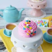 Pink fairy cake on a mini cake stand during a tea party.