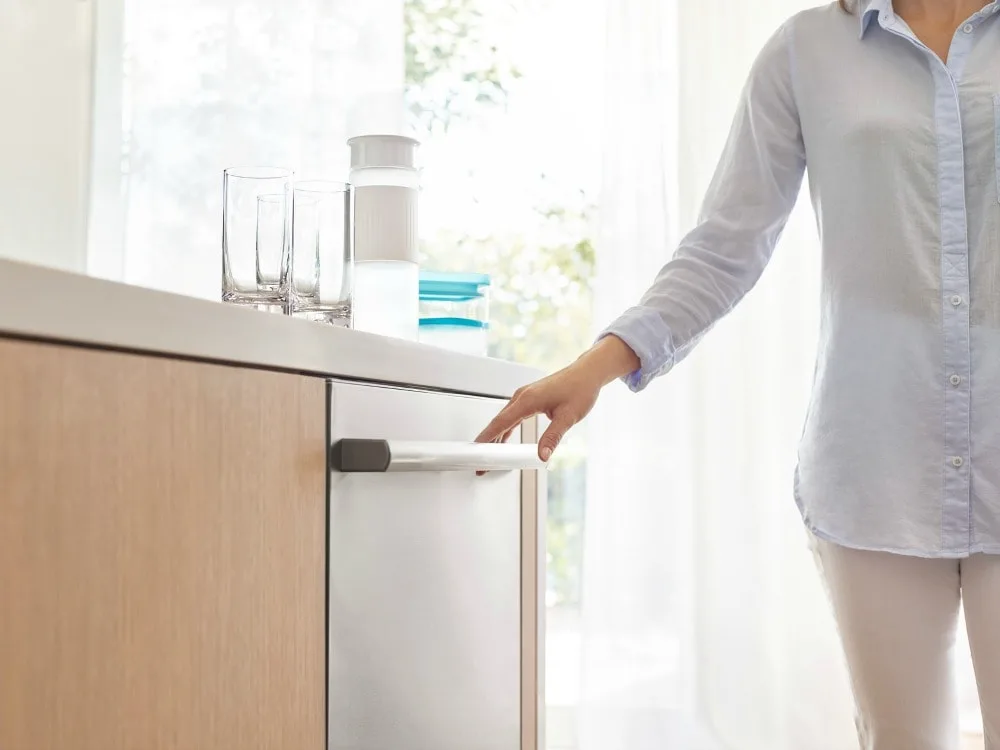 Person touching the handle of a dishwasher. 