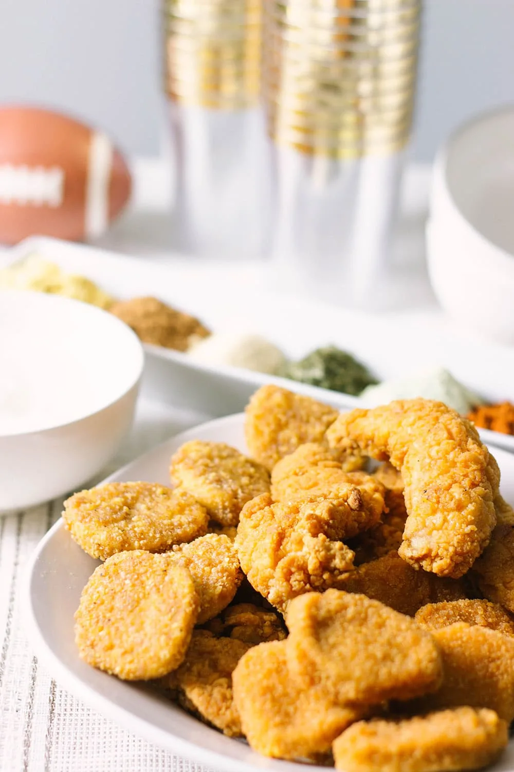 Chicken strips piled on a plate in front of glasses and seasonings. 