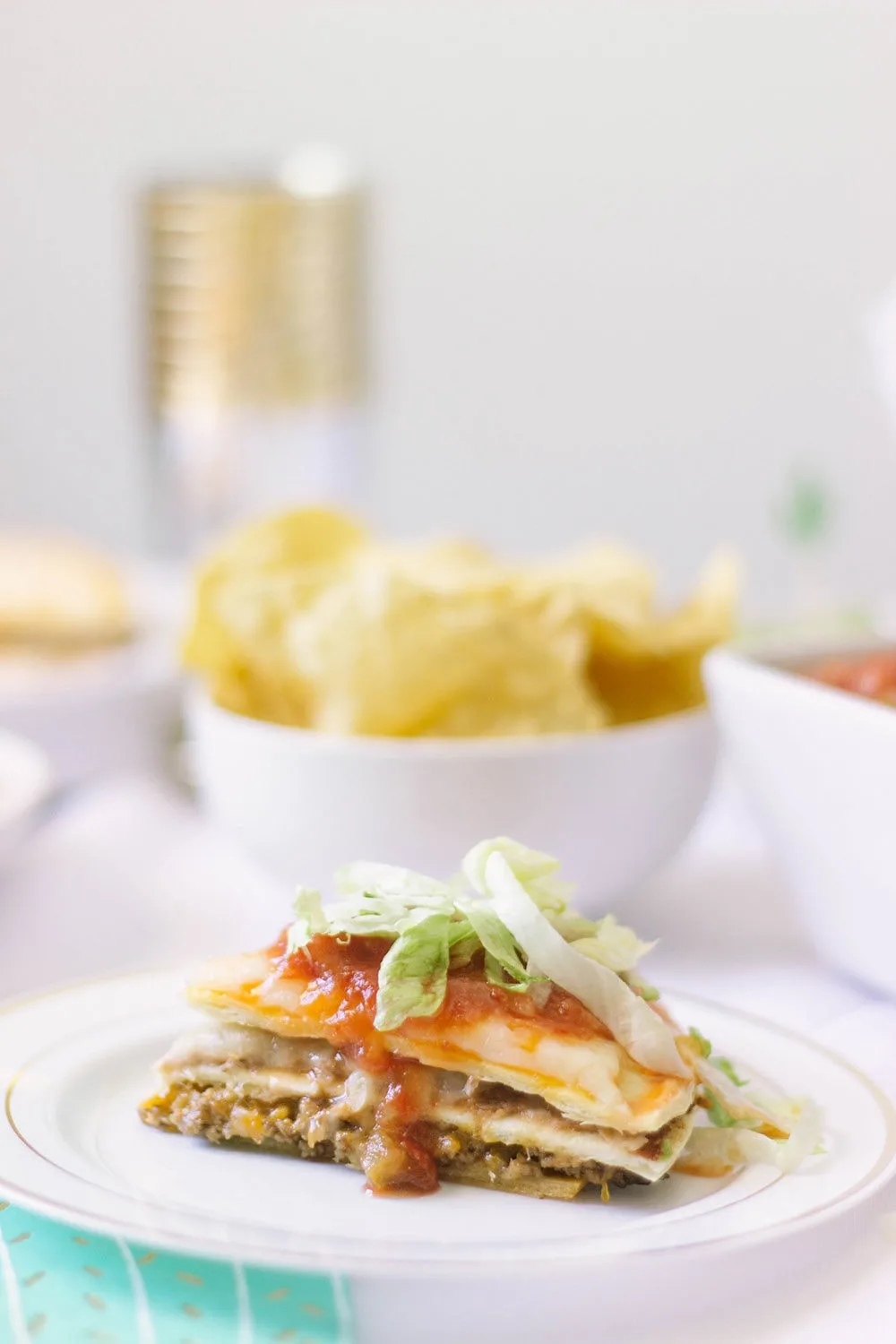 Taco pizza slice on a plate with a bowl of chips.