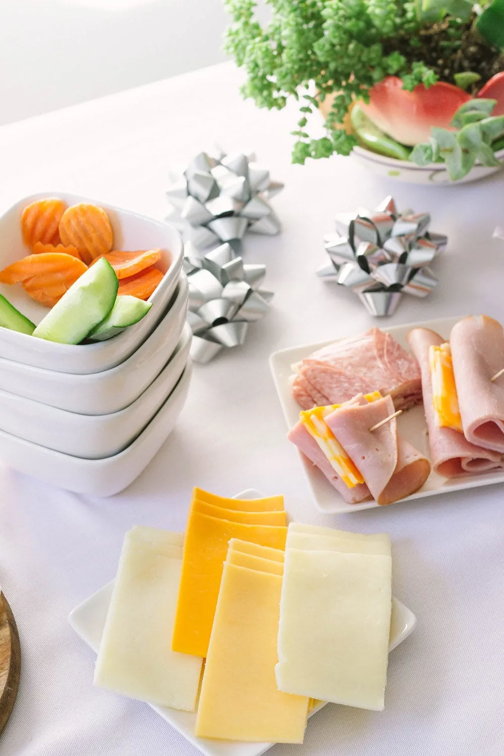 Cheeses on a plate, meat, and veggies on a table.