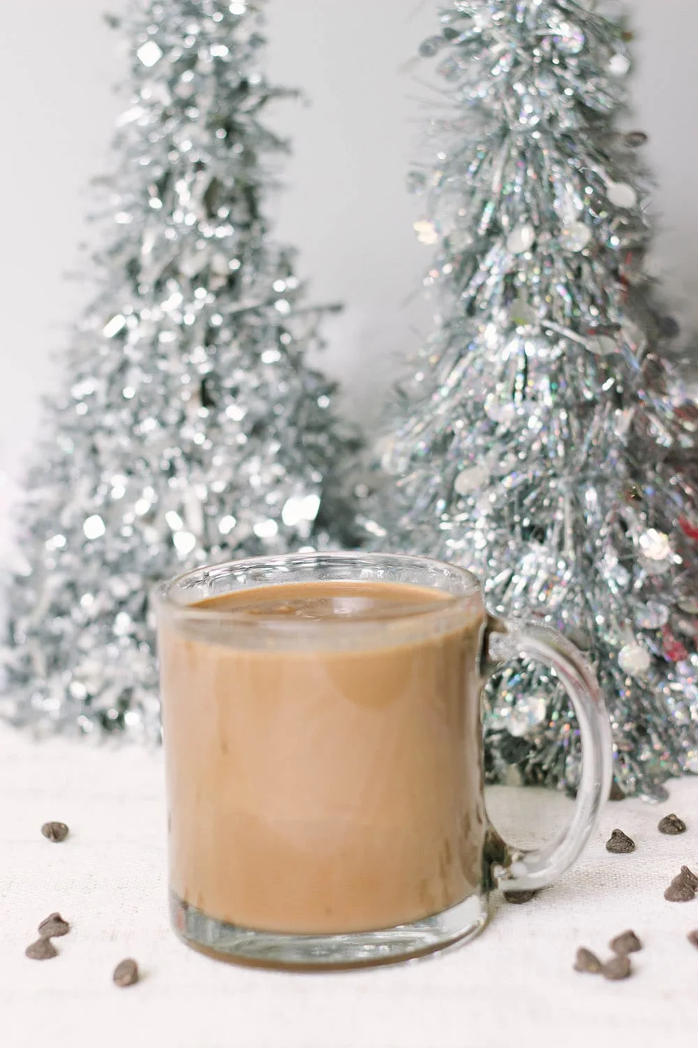 Glass of low carb hot chocolate in front of silver Christmas trees.