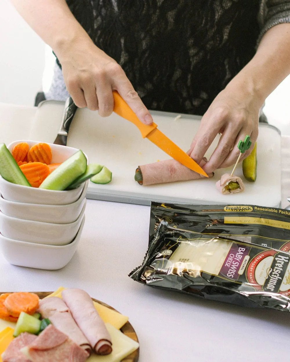 Cutting ham and pickle roll up snack with an orange knife. 