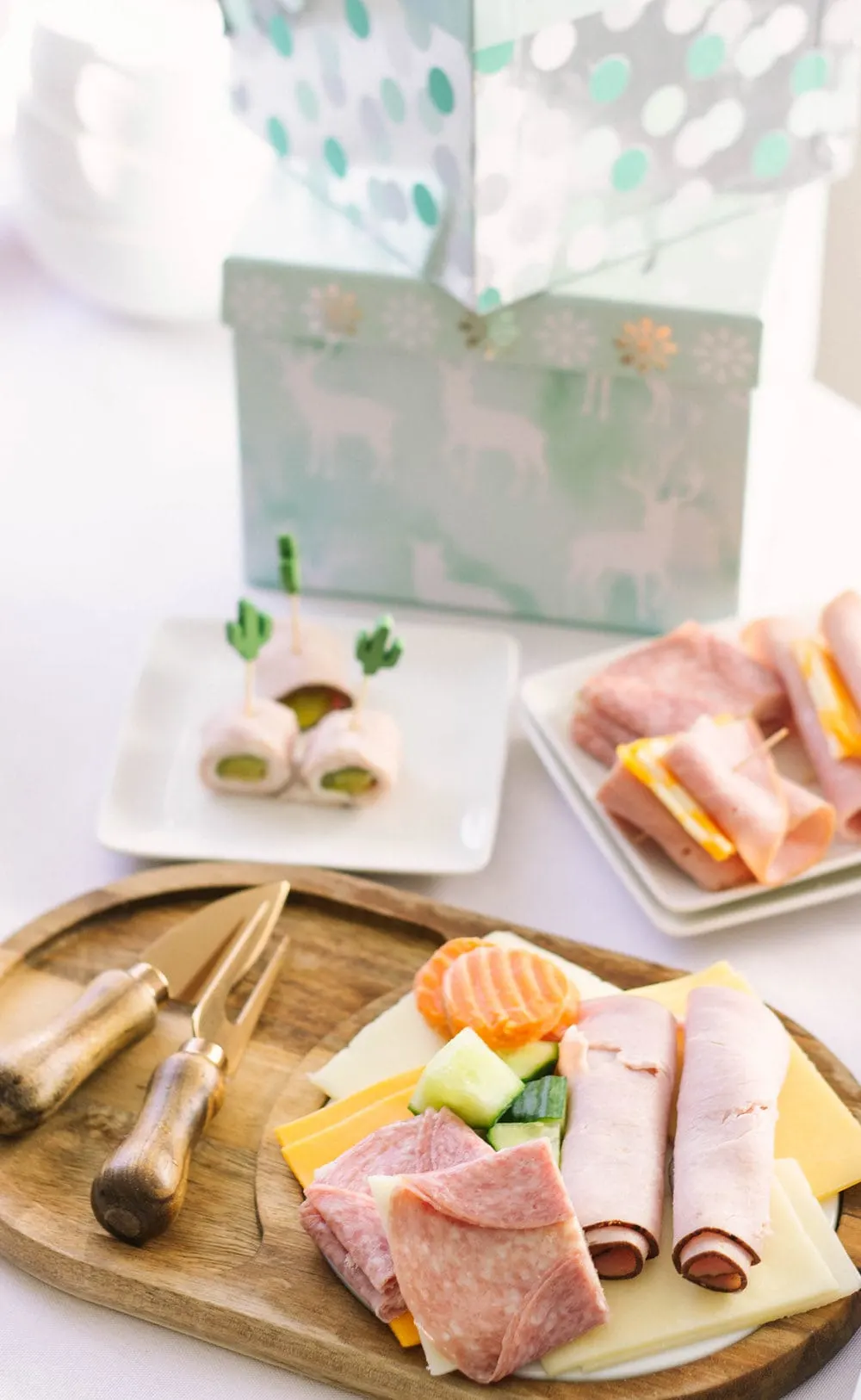 Meats and cheeses on a board and plates with gifts in the background. 