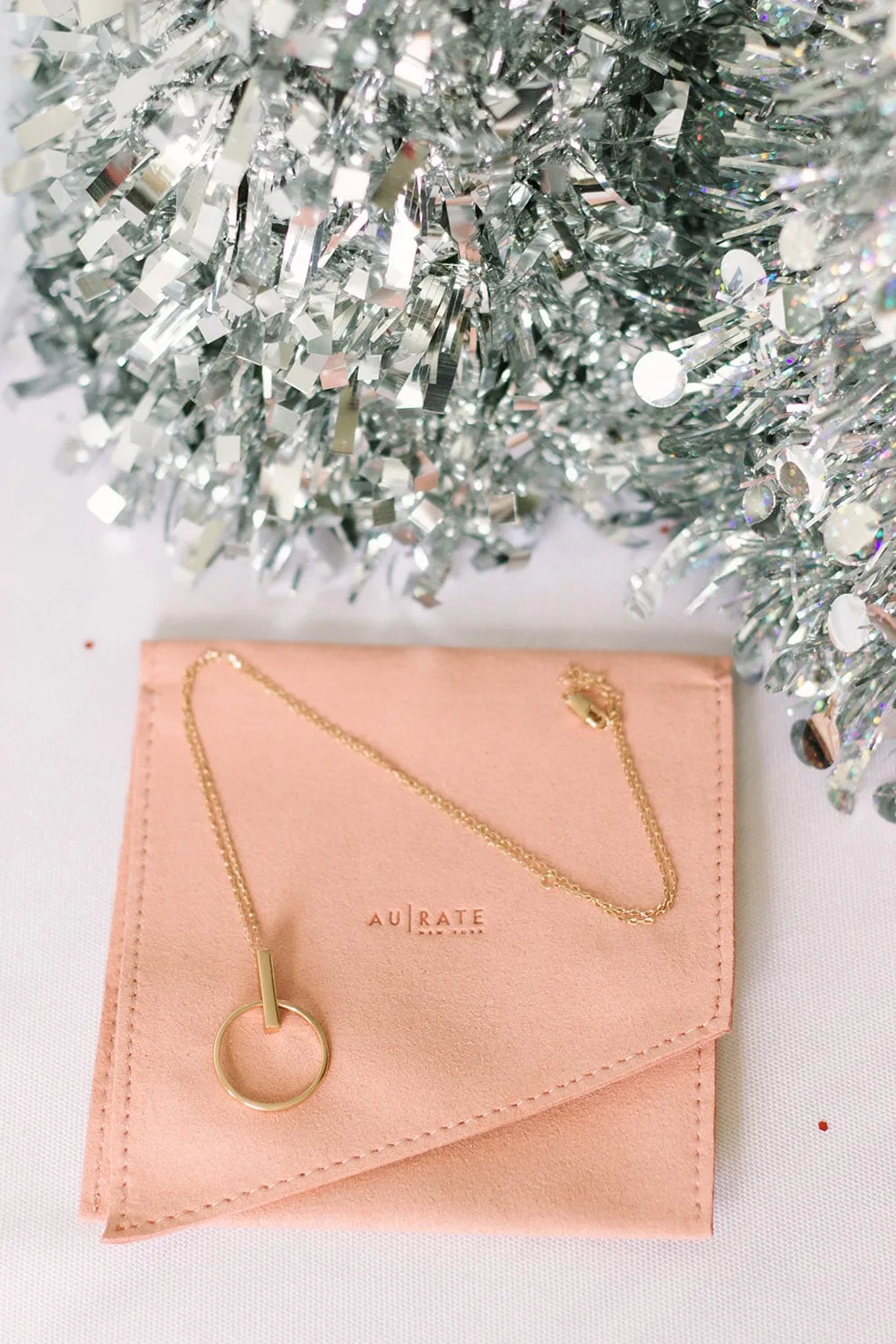 Rose gold necklace on an Aurate pouch under a silver tree. 