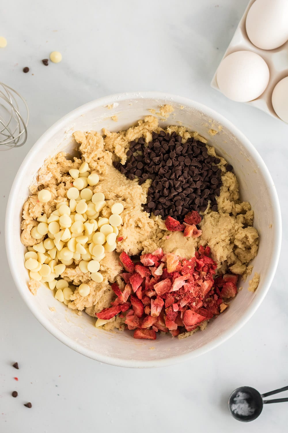 White and chocolate chips and freeze-dried strawberries in a mixing bowl with cookie batter. 