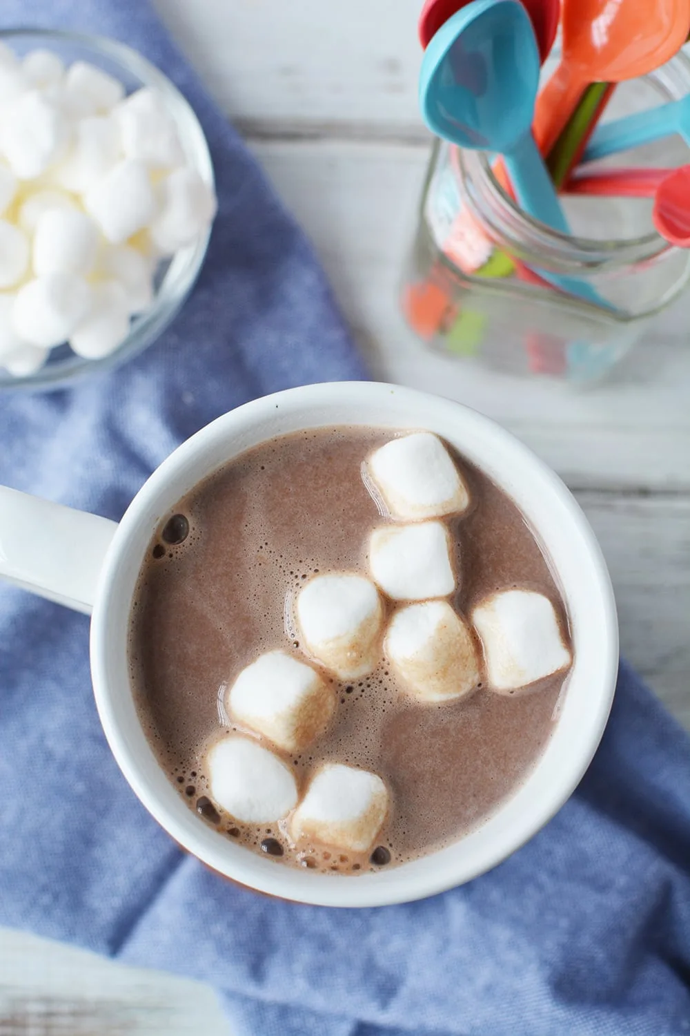 Cup of hot cocoa on a blue napkin with colorful spoons.