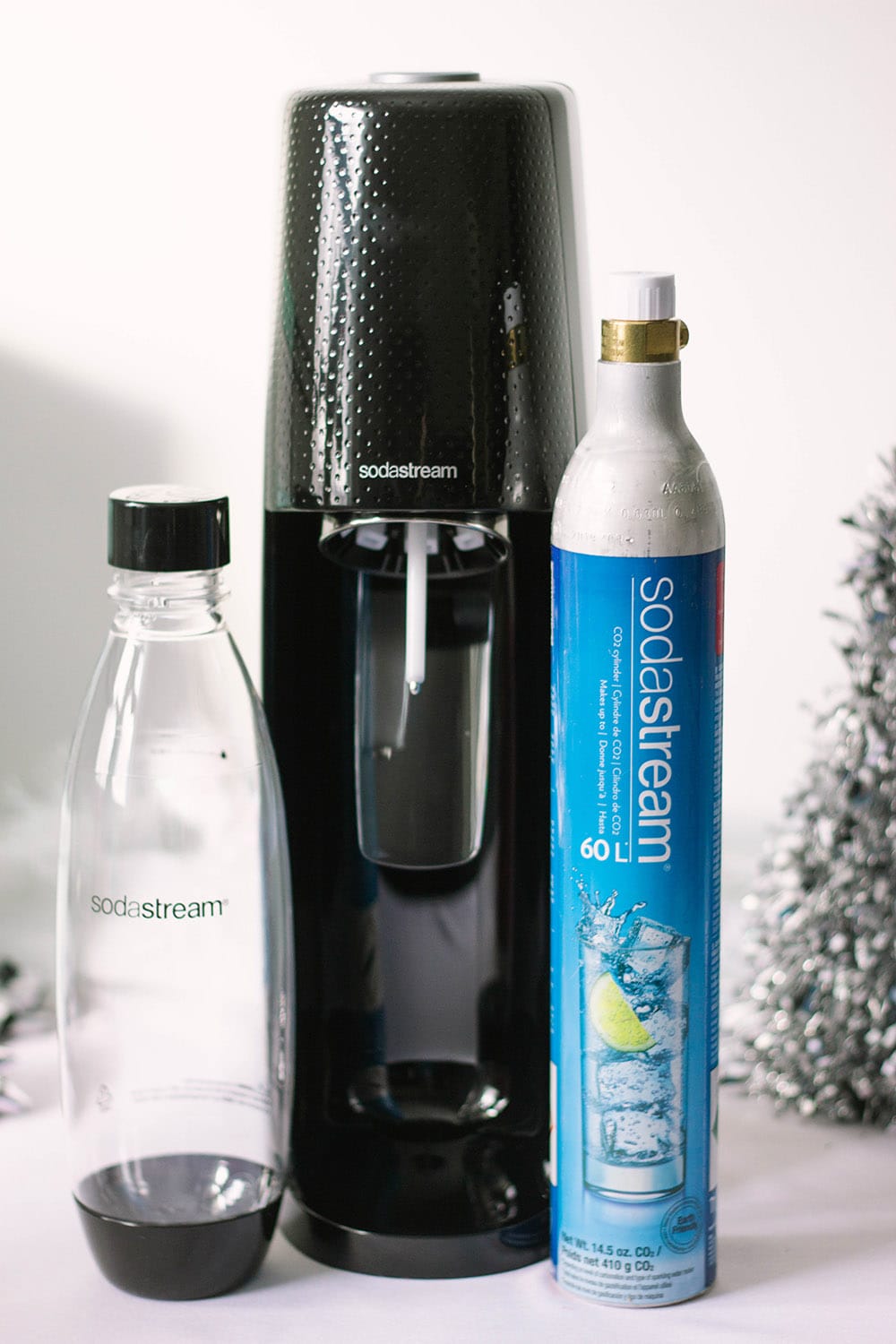 SodaStream machine with canister on a table with a silver tree. 
