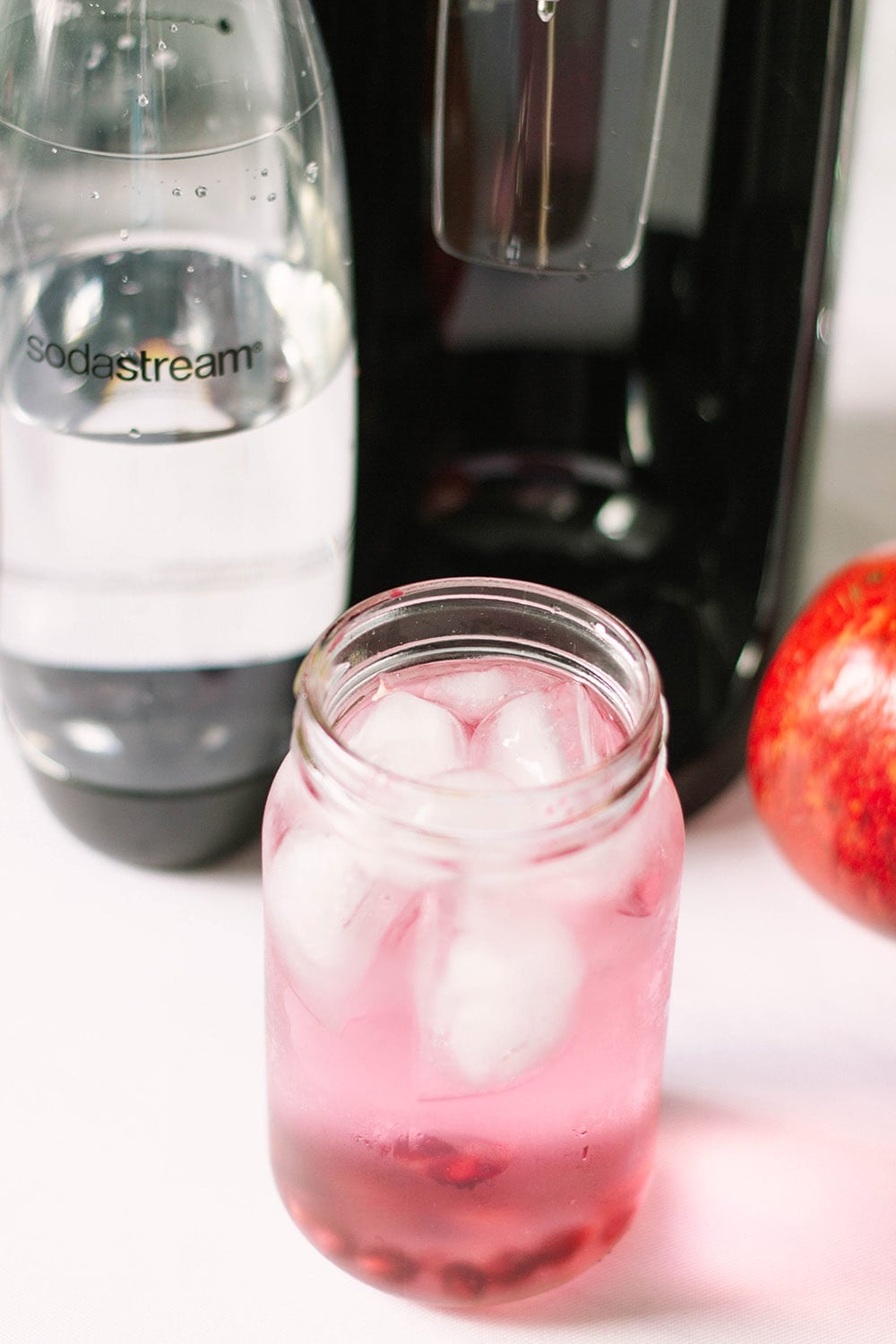 Red sparkling drink by a SodaStream machine and an apple. 