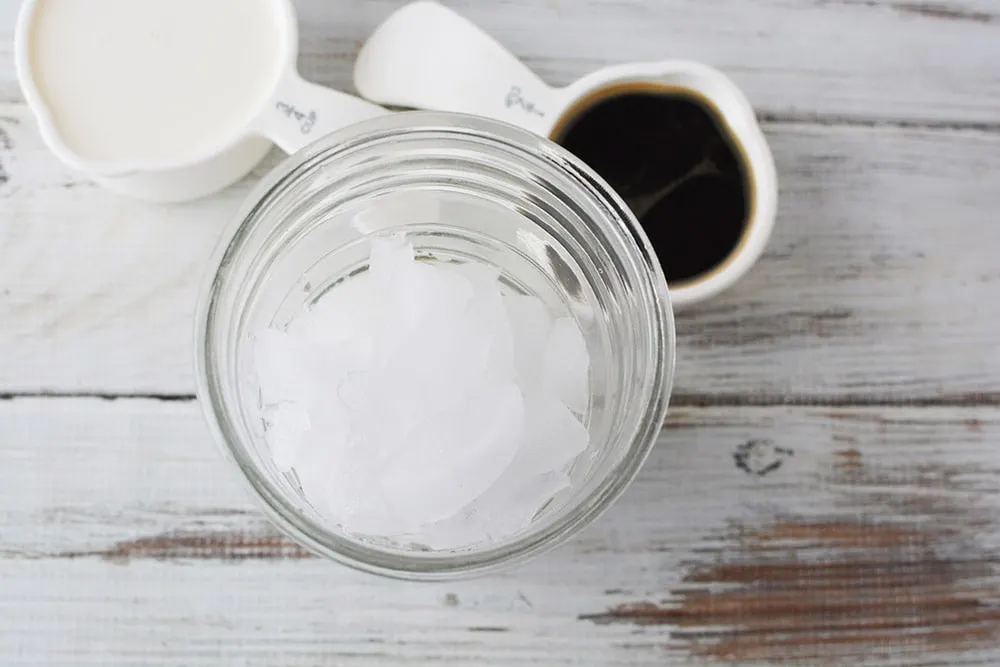 Ice in tumbler next to coffee. 