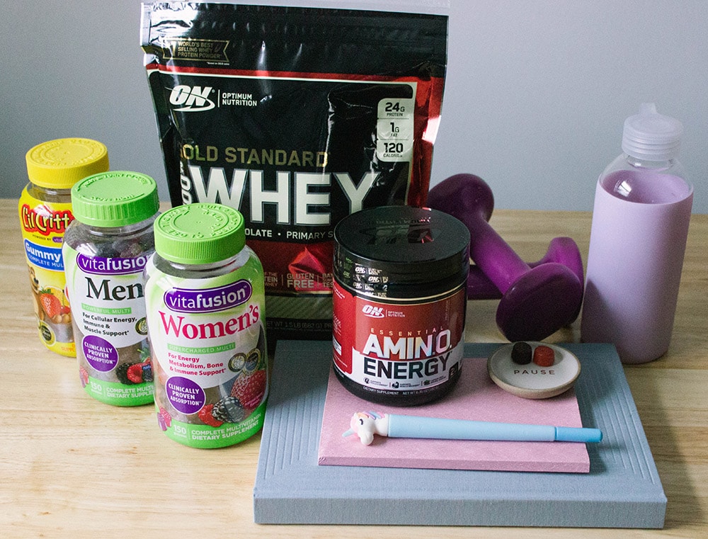 Protein powder, gummy vitamins, a water bottle, and notebooks on a desk. 
